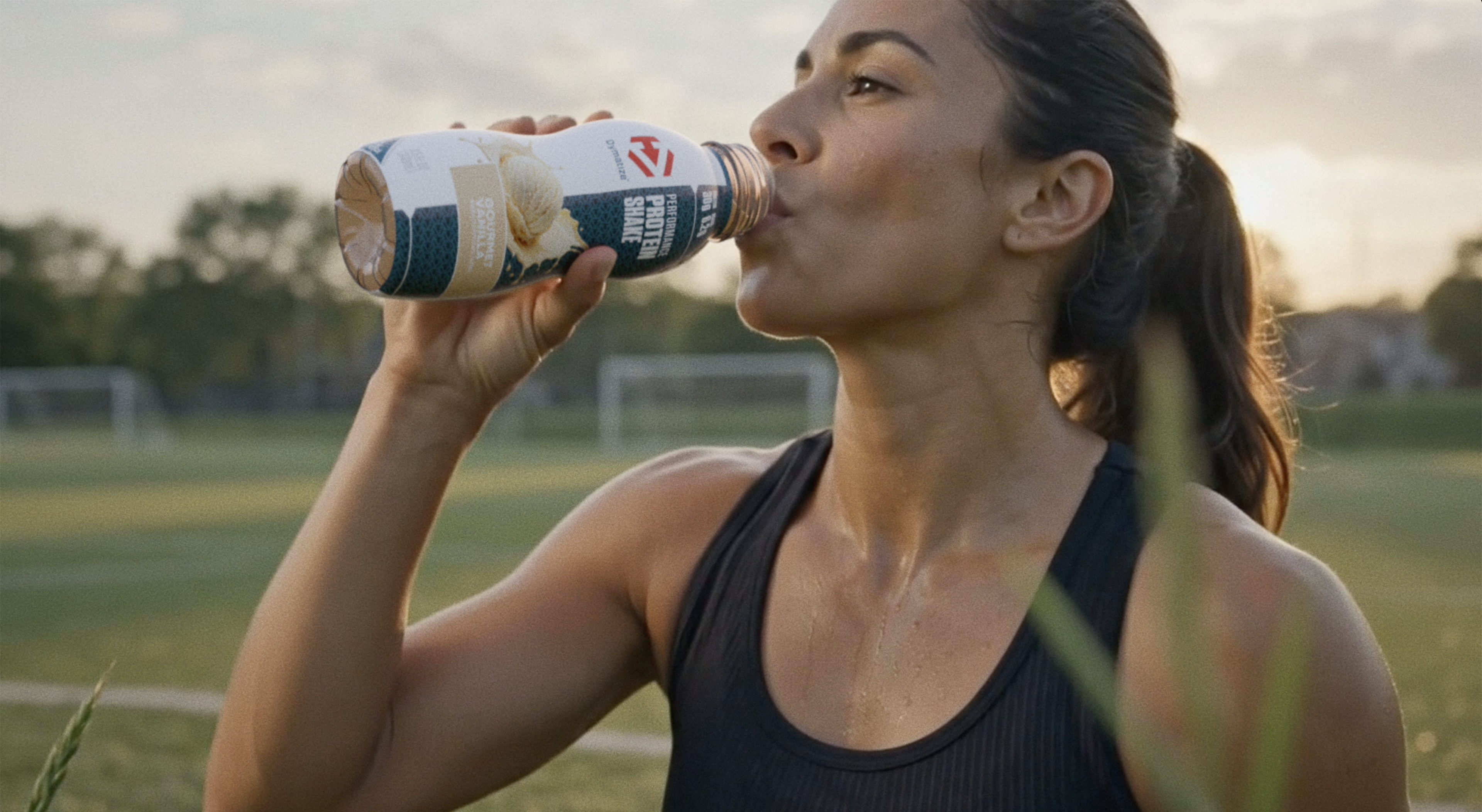 A woman drinking a Vanilla flavoried Dymatize Performance Protein shake after a workout.