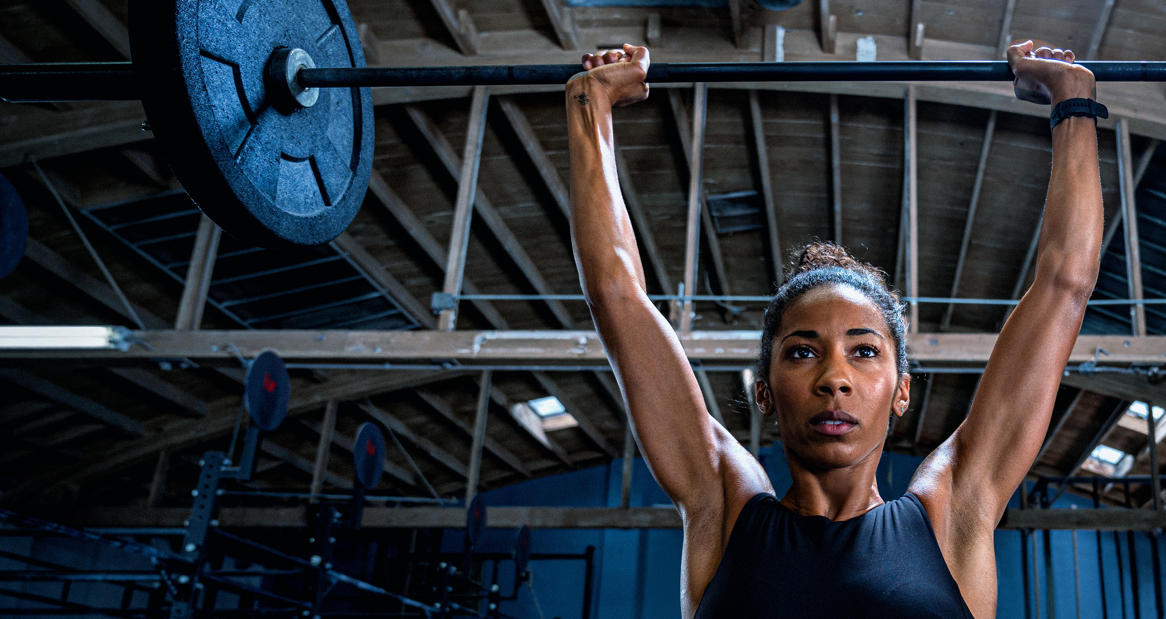 Una mujer en el gym, levantando una pesa sobre su cabeza.