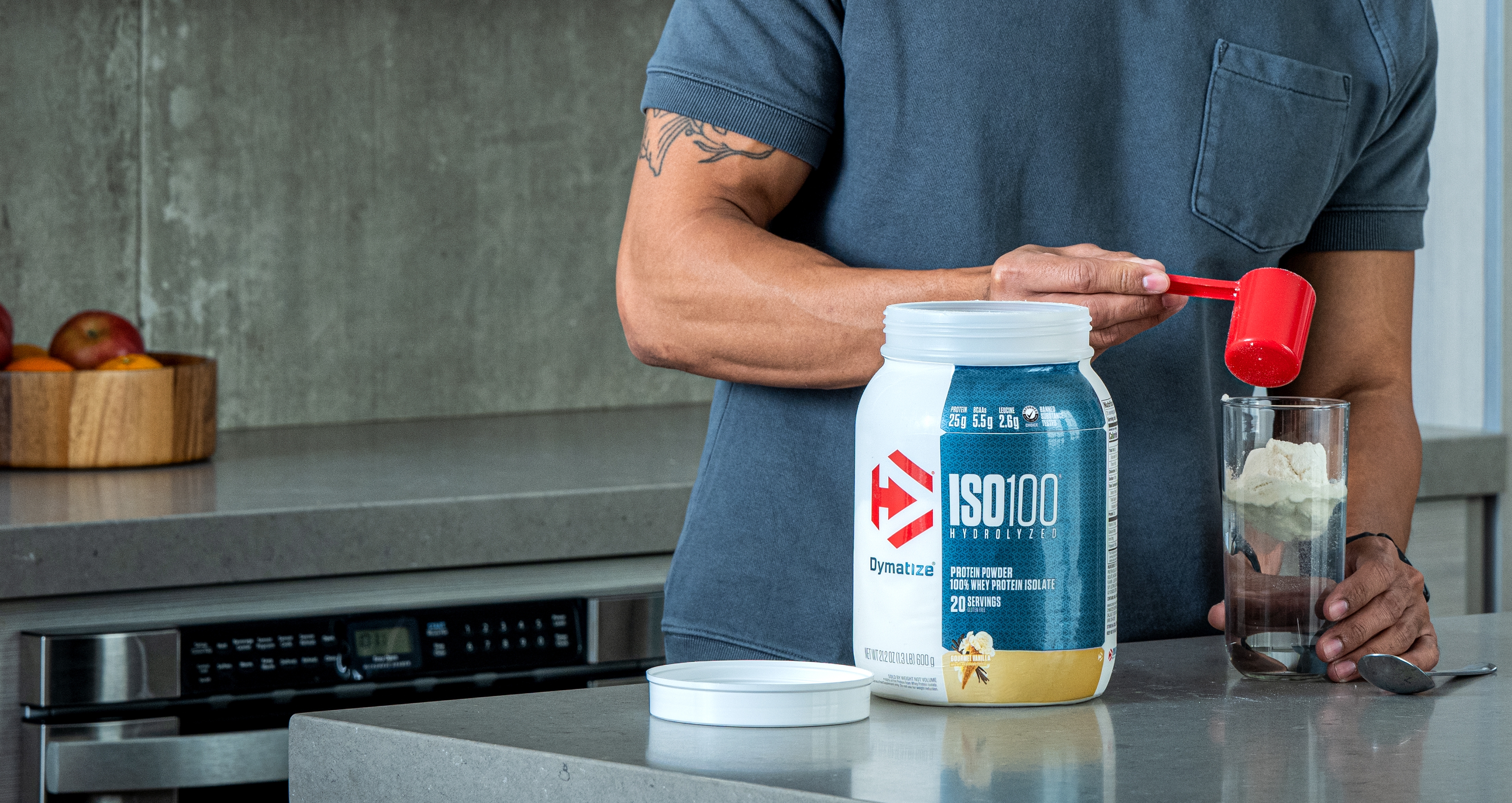 A man in a kitchen pouring Dymatize ISO100 Whey Protein into a glass.