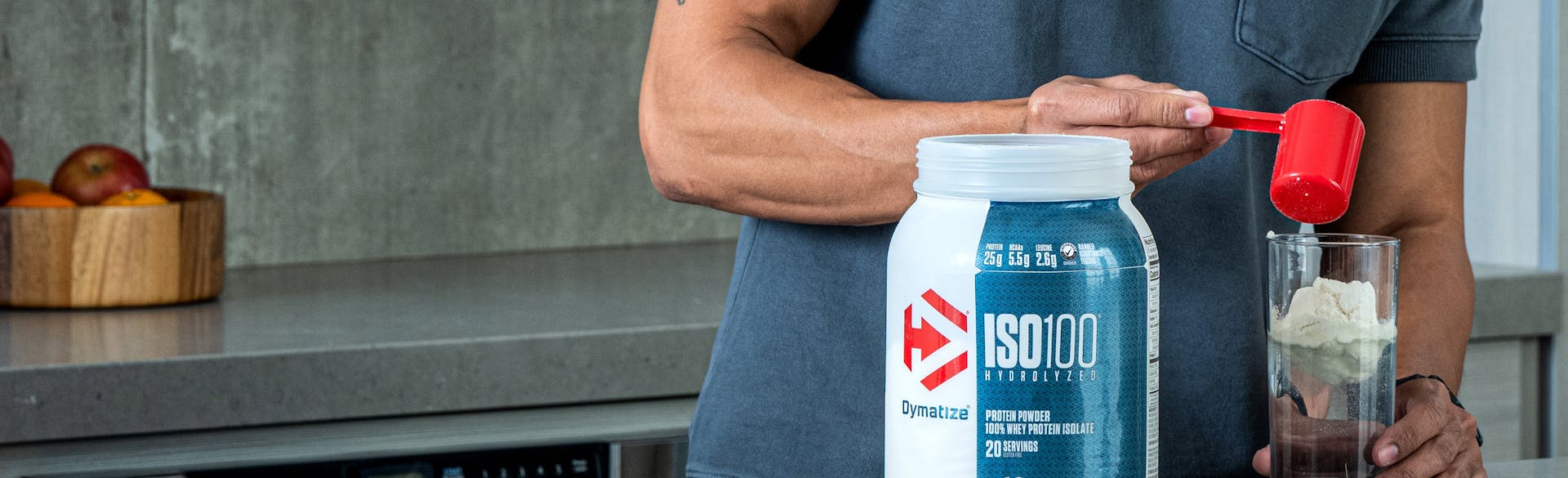 A man in a kitchen pouring Dymatize ISO100 Whey Protein into a glass.